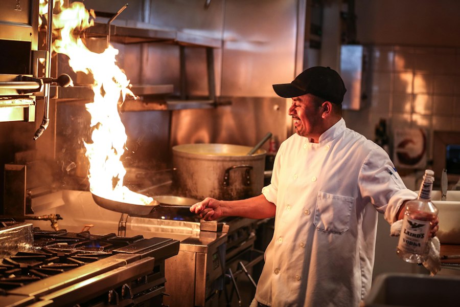 A chef cooking over a flame in a busy kitchen